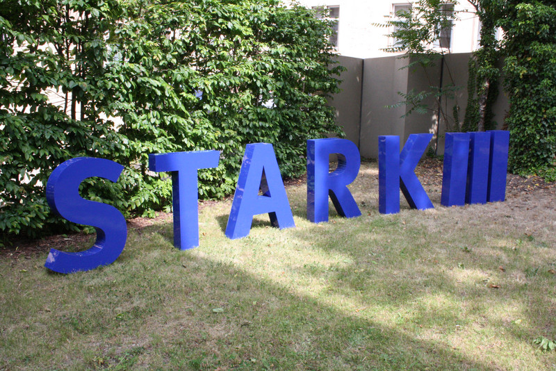 Einzelbuchstaben und -ziffern stehen auf einer Wiese und ergeben das STARK III - Logo